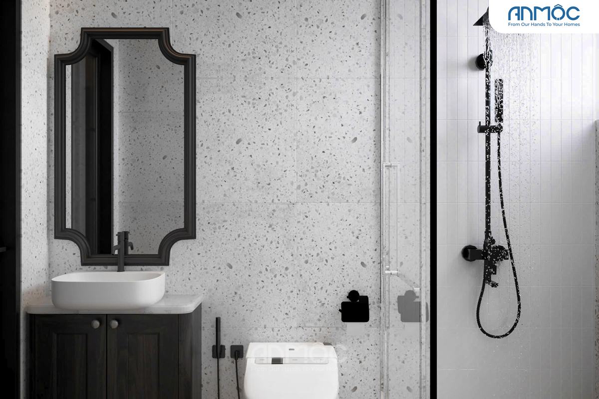 Phòng vệ sinh với lavabo trắng đặt trên tủ gỗ đen, gương khung đen kiểu cách và tường ốp gạch terrazzo trắng