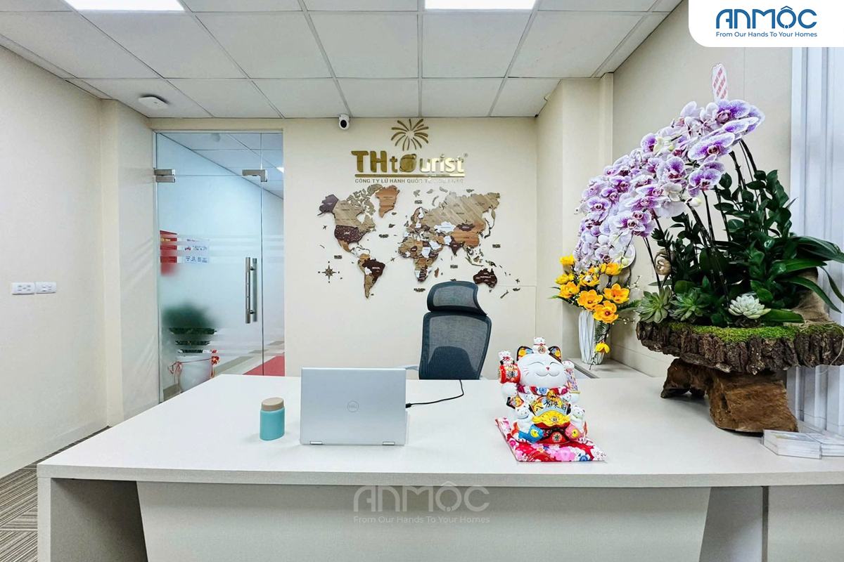 Cận cảnh bàn làm việc lễ tân với máy tính xách tay và một bản đồ thế giới lớn trang trí trên tường phía sau, cùng một chậu hoa lan lớn