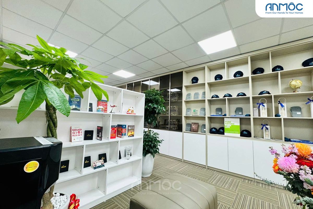 Khu vực thư viện nhỏ với giá sách trắng chứa nhiều đầu sách và sản phẩm trưng bày, nằm cạnh tủ kệ trưng bày mũ và quà lưu niệm